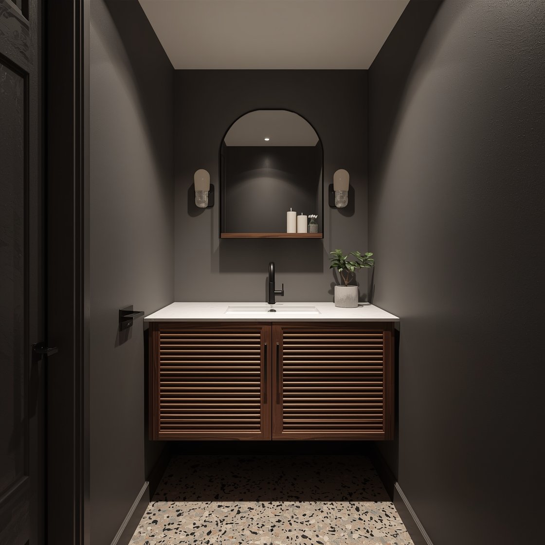 Medium corner-angle photorealistic shot of a moody powder room with soft charcoal walls and bright white ceiling; teak vanity with slatted doors and a slim-profile integrated sink; terrazzo floor with warm neutrals and black chips; matte black faucet and arched black-framed mirror; single opal globe sconce centered above; narrow floating teak shelf with candles and matches; petite snake plant in a cement pot on the toilet tank. High-contrast lighting that feels like a chic hotel, no people.
