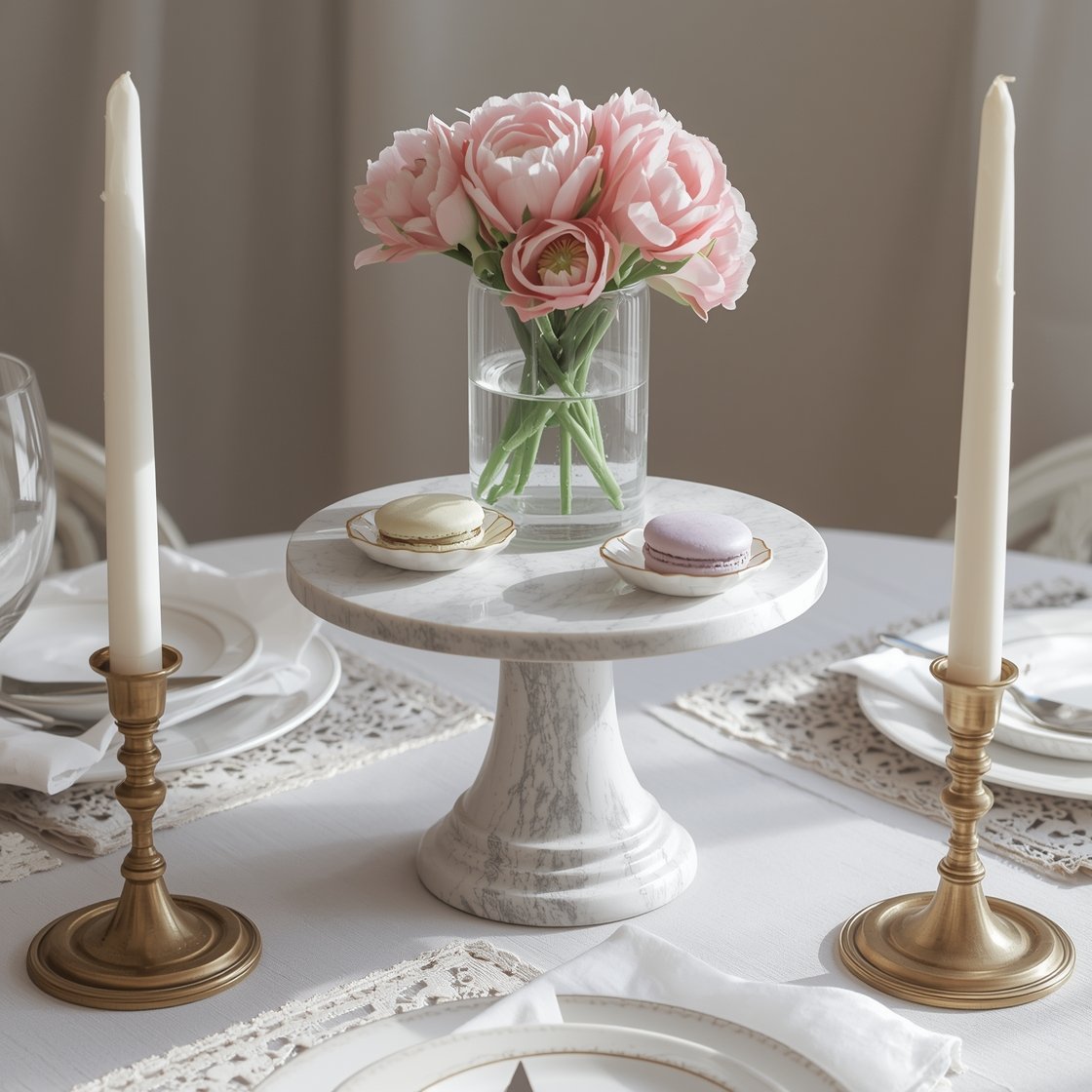 Photorealistic closeup, slightly elevated angle on a Parisian-inspired centerpiece: two stacked marble cake stands at the center of a table. On the top tier, a clear cylinder vase filled with pale pink ranunculus. On the lower tier, small ceramic dishes hold macaron pastels in lavender, pistachio, and rose. Two brass taper holders frame the scene. Delicate lace placemats run widthwise beneath the stands. Refined, feminine ambiance with soft, diffused café-style daylight.